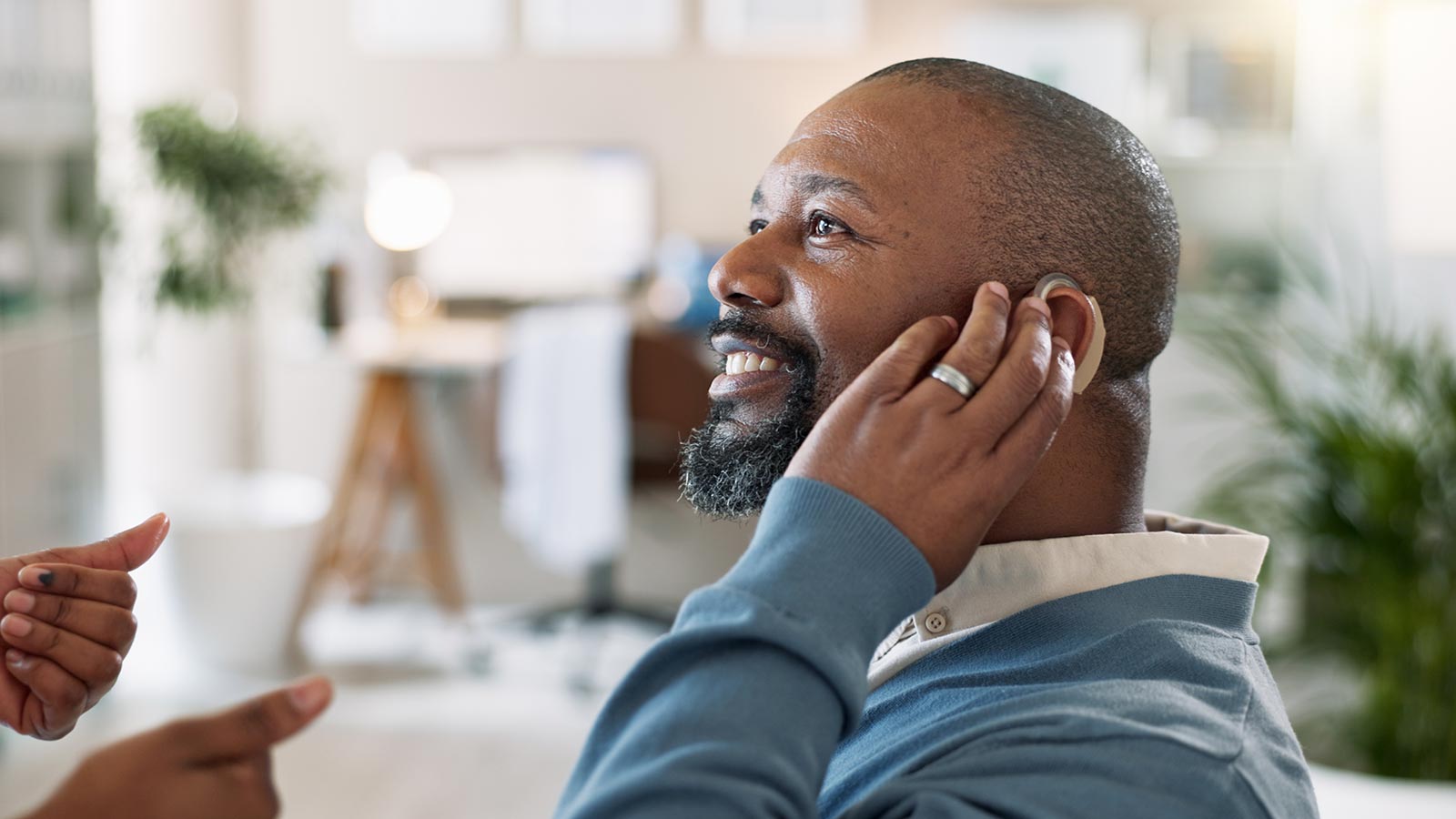 Man holding hand up to ear to adjust hearing aid.