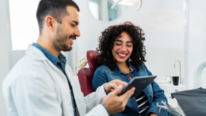 Patient in chair smiling at provider who is pointing at tablet.