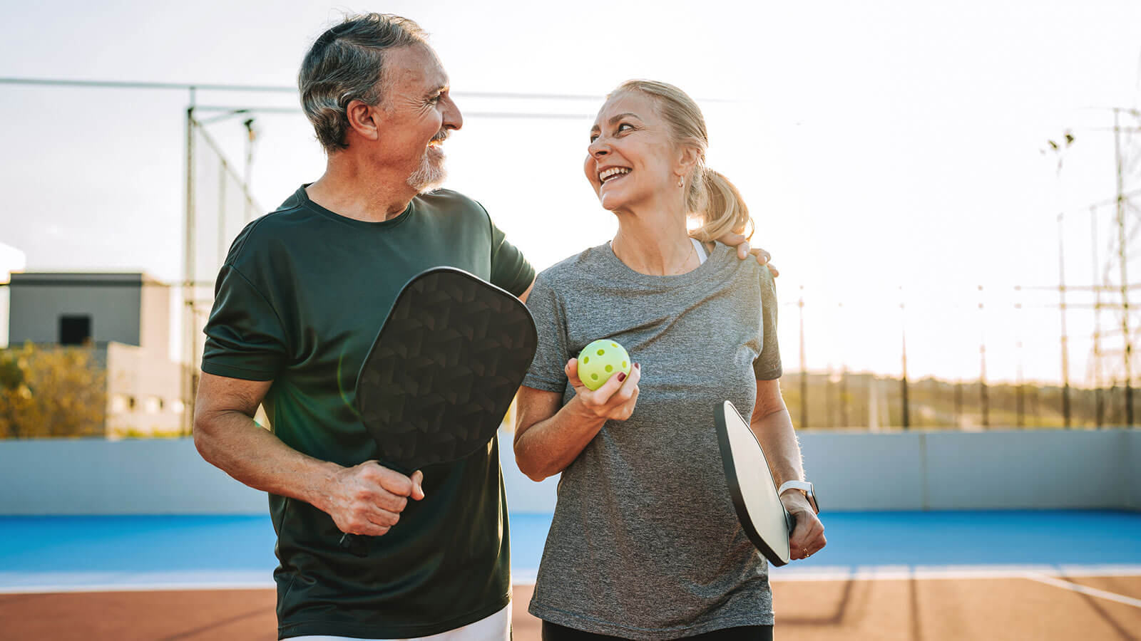 A husband and wife in their late 60s walk off a pickleball court enjoying their retirement hobby.