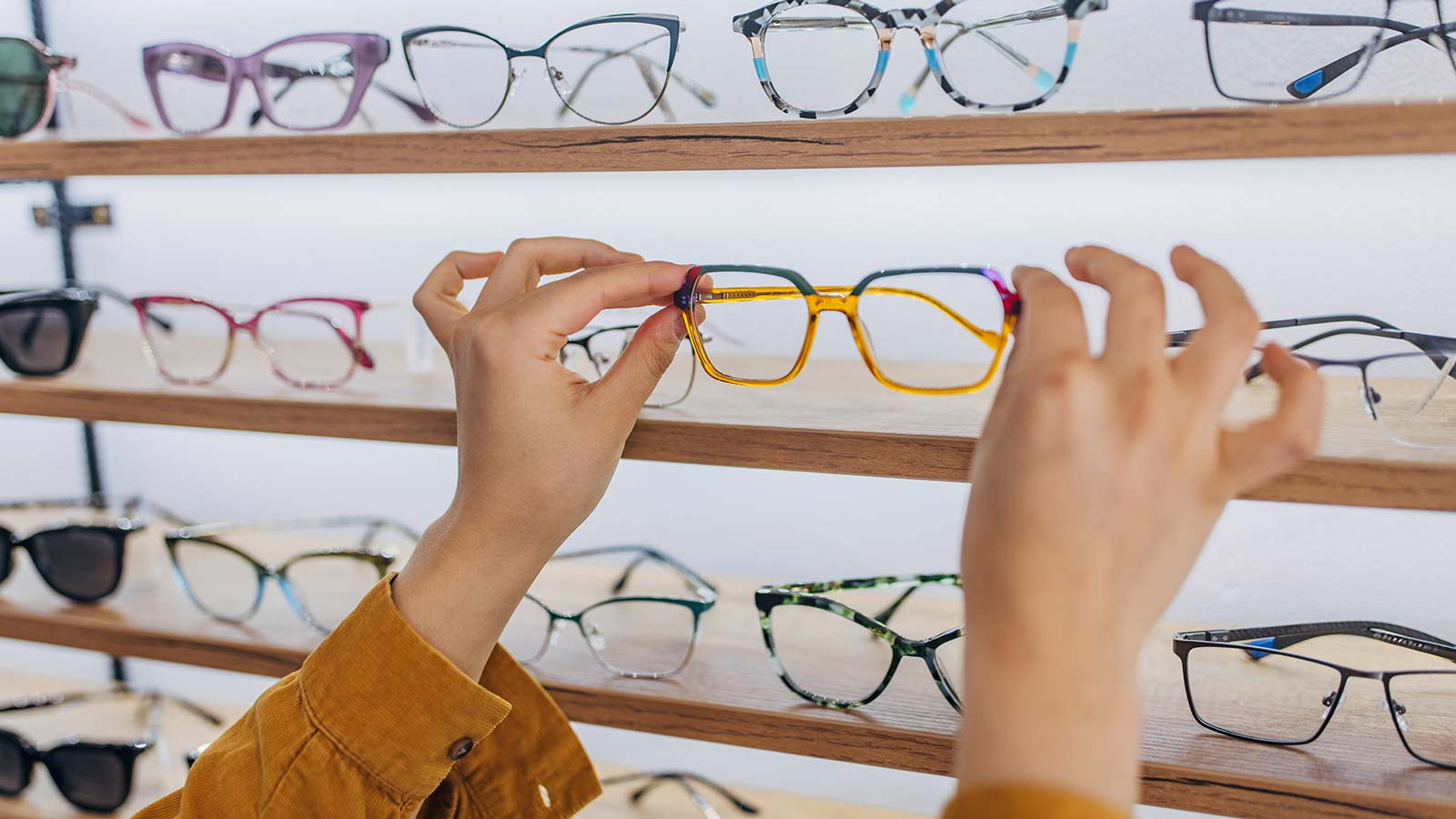 Hands picking up eye glasses off of a shopping display.