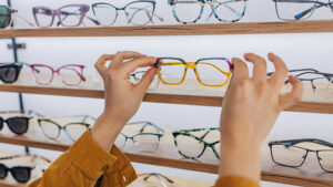 Hands picking up eye glasses off of a shopping display.