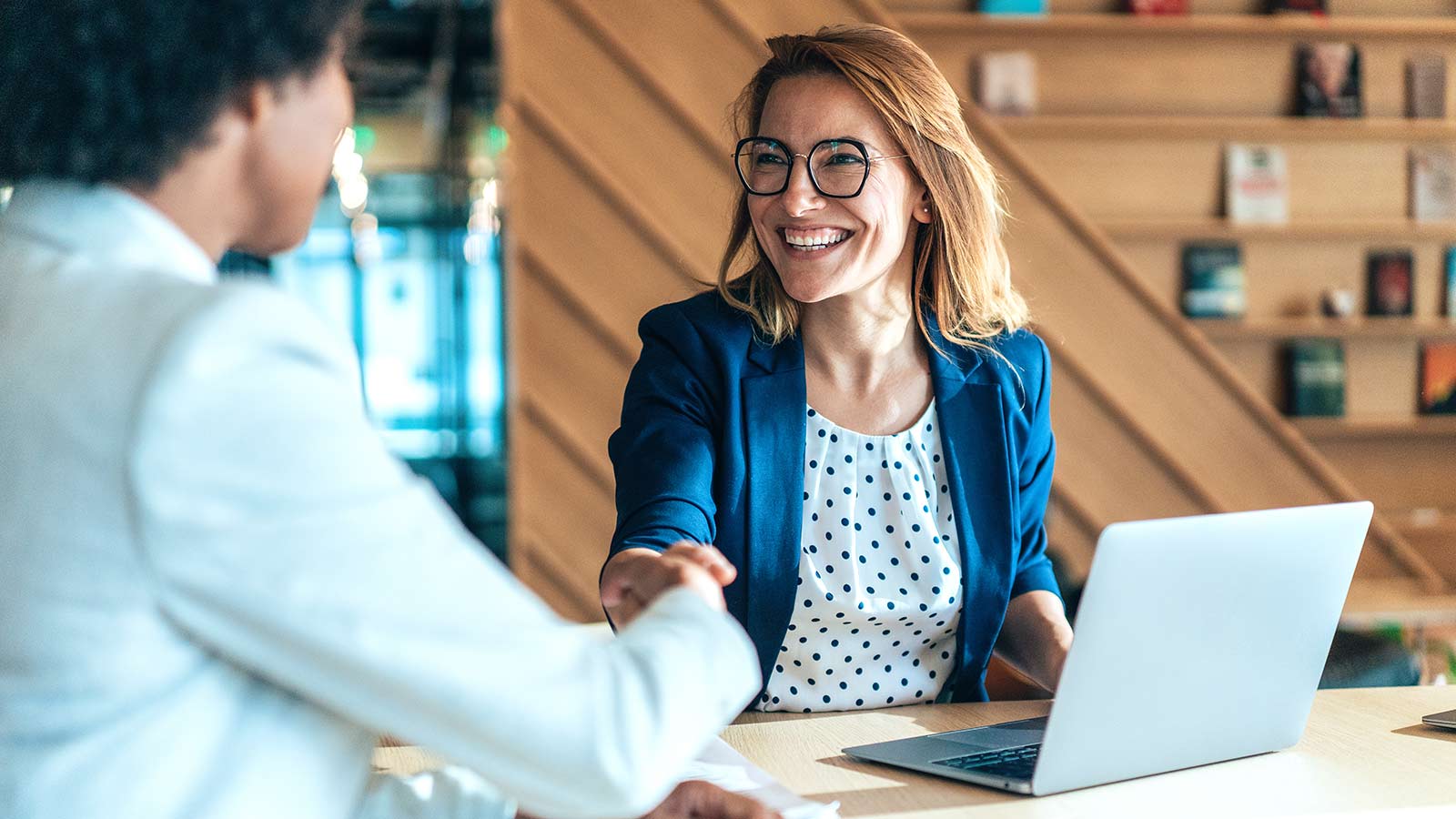Two people shaking hands while sitting at a table during a business meeting.
