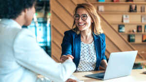 Two people shaking hands while sitting at a table during a business meeting.