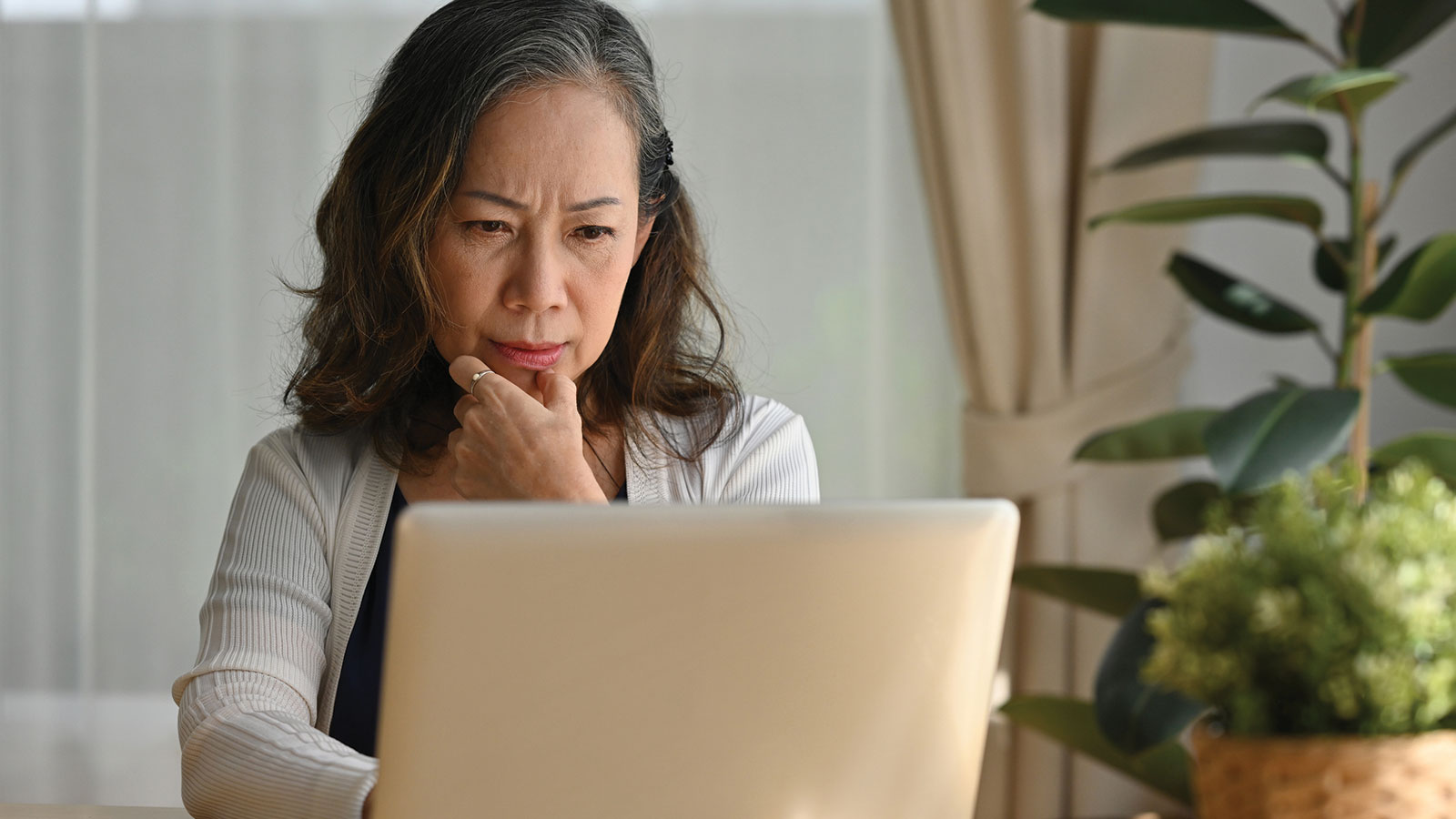 A woman sitting at a laptop with hand on chin, reviewing information during election season, illustrating uncertainty around whether to invest before or after an election.