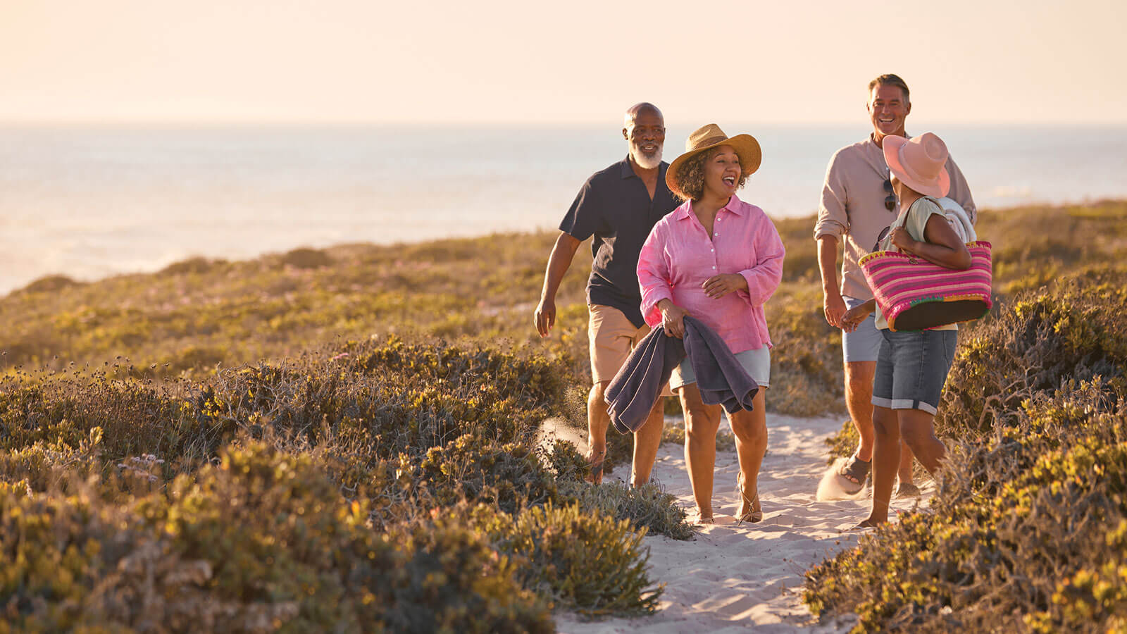 Two couples in their late 50s are on vacation, laughing as they leave the beach after a fun day.
