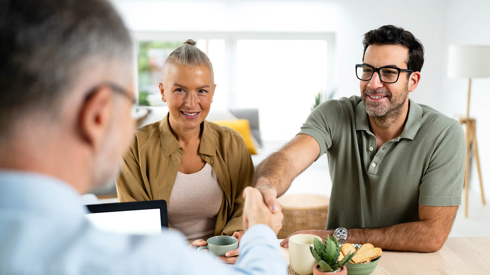A financial professional meets with two clients at a table, shaking hands during an in-person discussion.