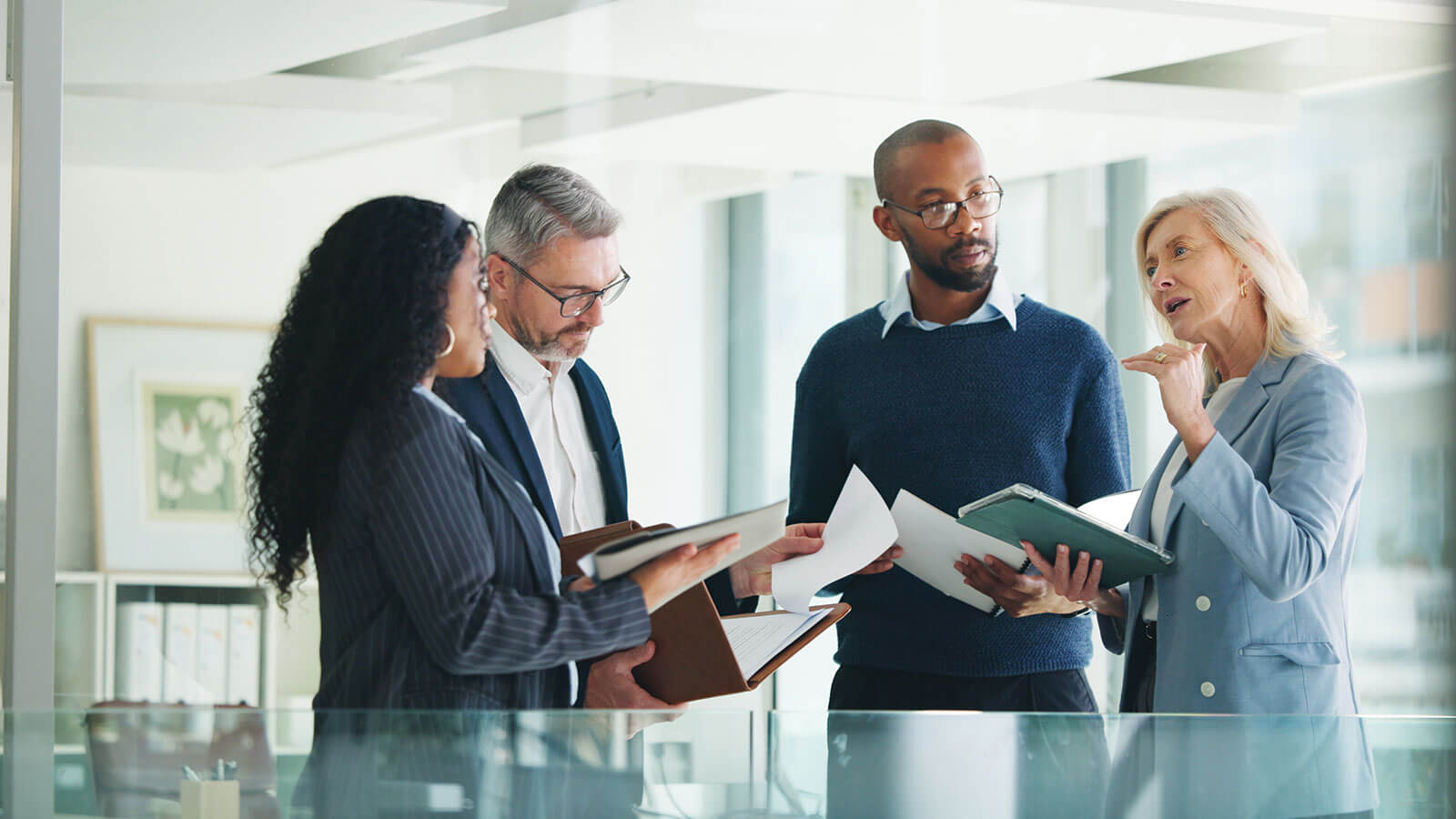 Four staff members from a financial firm are standing in an office discussing financial strategy options to help support a financial professional.