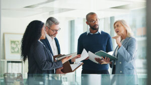 Four staff members from a financial firm are standing in an office discussing financial strategy options to help support a financial professional.